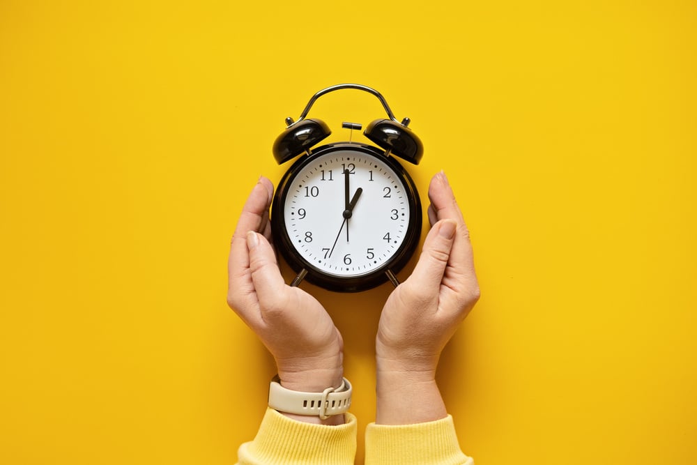 Daylight saving day. Fall Back. Black Alarm clock and female hands on yellow background. Daylight saving time end