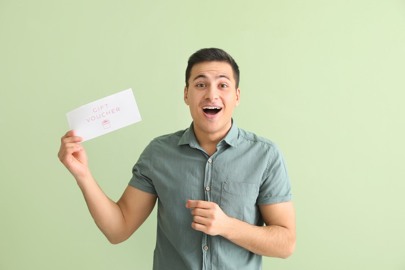 Surprised Young Man with Gift Voucher on Color Background